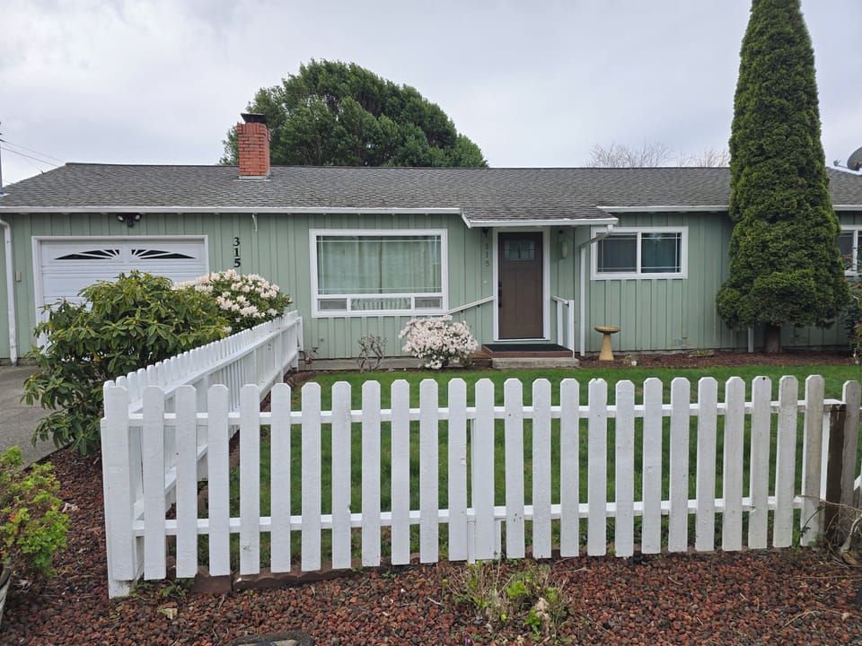 Charming cottage with picket fence, lush lawn, and cozy porch