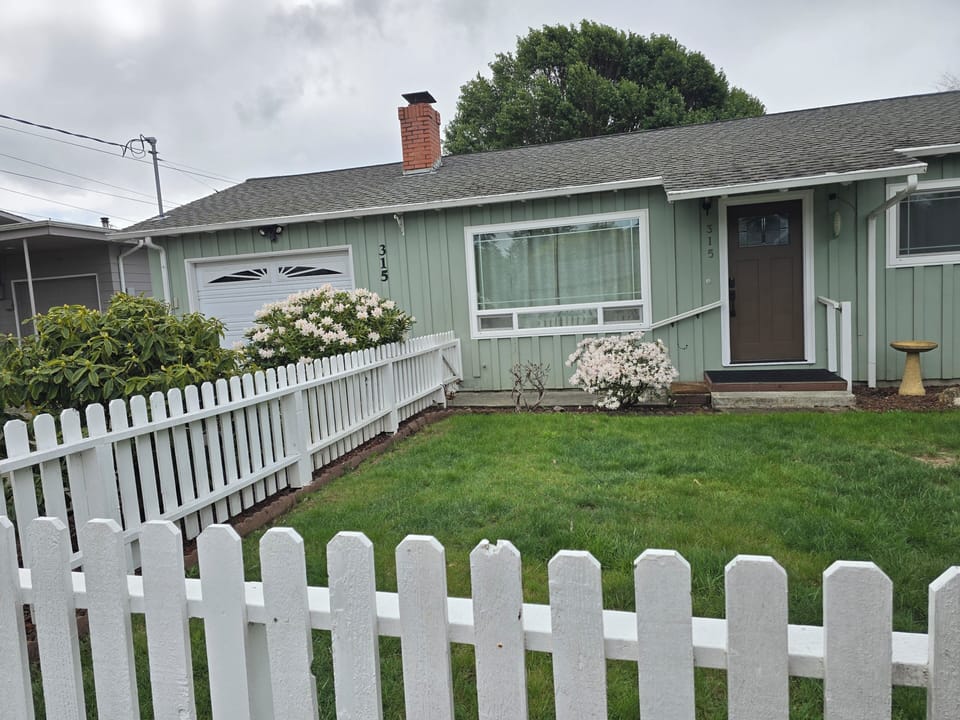 Charming cottage with picket fence, lush lawn, and picture window