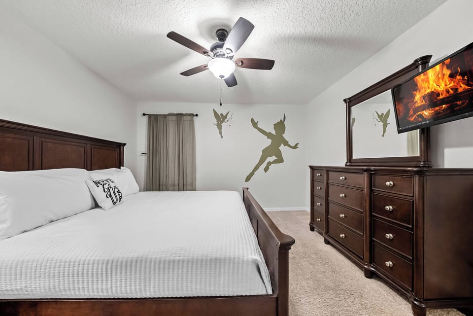 Enjoy restful nights in this inviting bedroom with a plush king-size bed and warm wooden furniture. The soft beige carpet adds comfort, and the ceiling fan provides a gentle breeze for a cozy atmosphere.