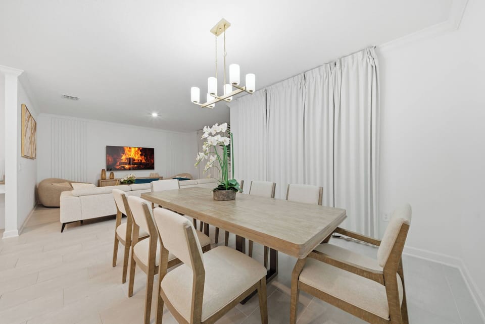 Experience delightful dining in a cozy space with a stylish wooden table and upholstered chairs, where soft tones, elegant drapery, and a modern chandelier create a relaxing and sophisticated atmosphere just for you.