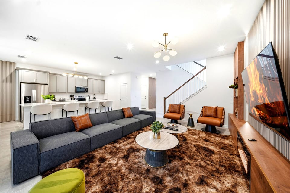 Enjoy a stylish living area featuring a cozy gray sectional and elegant leather armchairs for your comfort. The warm wooden accents and chic round coffee table add charm, while bright lighting creates an inviting atmosphere.