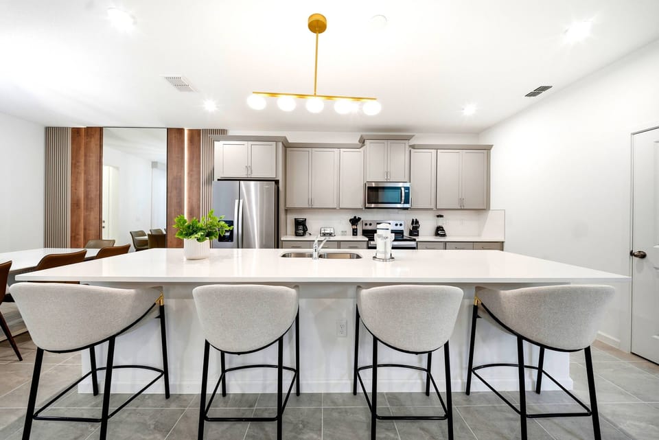 Welcome to this stylish kitchen featuring sleek gray cabinetry and a spacious quartz island, perfect for casual meals or morning coffee. The warm wood accents and modern lighting create a cozy, inviting atmosphere just for you.