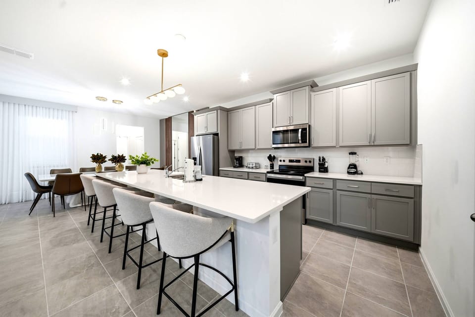 Experience a stylish kitchen with chic gray cabinetry and a spacious island for casual meals. The bright, airy atmosphere, filled with natural light from sheer curtains, makes this an inviting space for you and your guests.