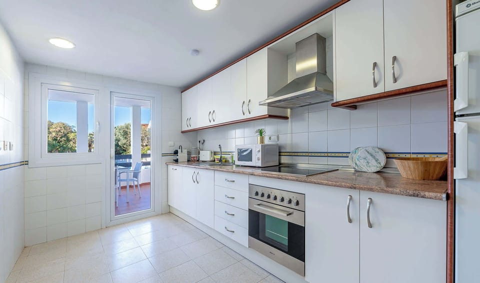 Modern kitchen with white cabinetry, stainless appliances, and tiled floors. Bright natural light enhances the clean, functional design.