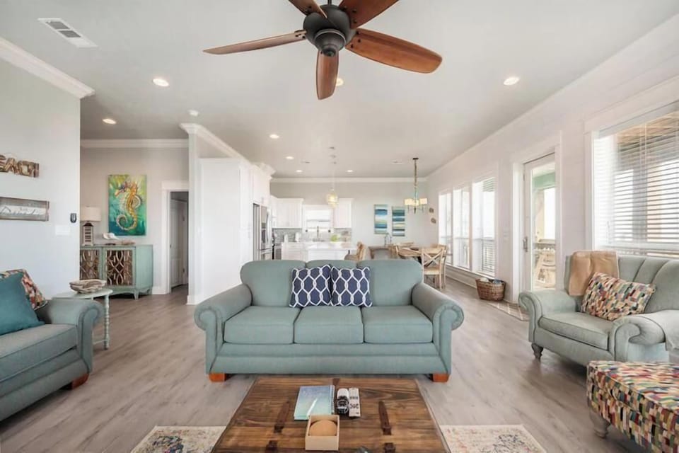 Relax in this sun-filled open-concept living space, designed for comfort and connection. With cozy seating, coastal accents, and seamless flow into the kitchen and dining area, it’s the perfect spot to unwind after a day of adventure.