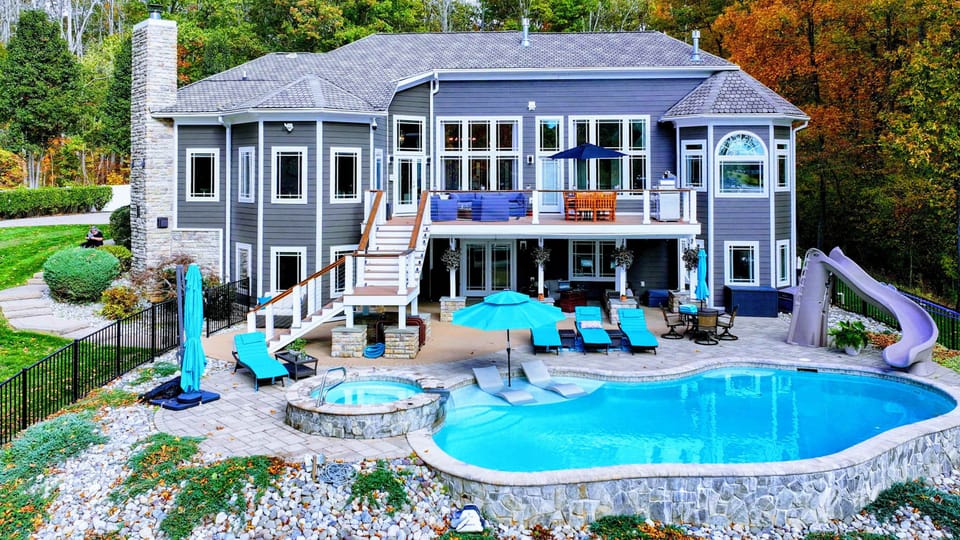 Resort-style heated pool with a built-in spa shelf and baja loungers in the water, framed by full lake views.