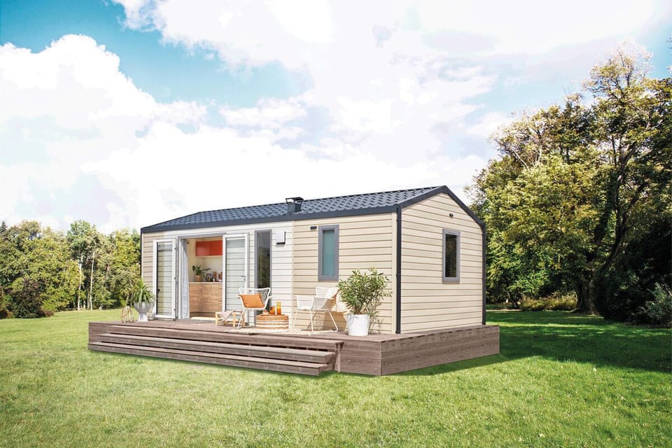 The modern exterior features a charming wooden deck, inviting seating, and a stylish design set within a lush green landscape.