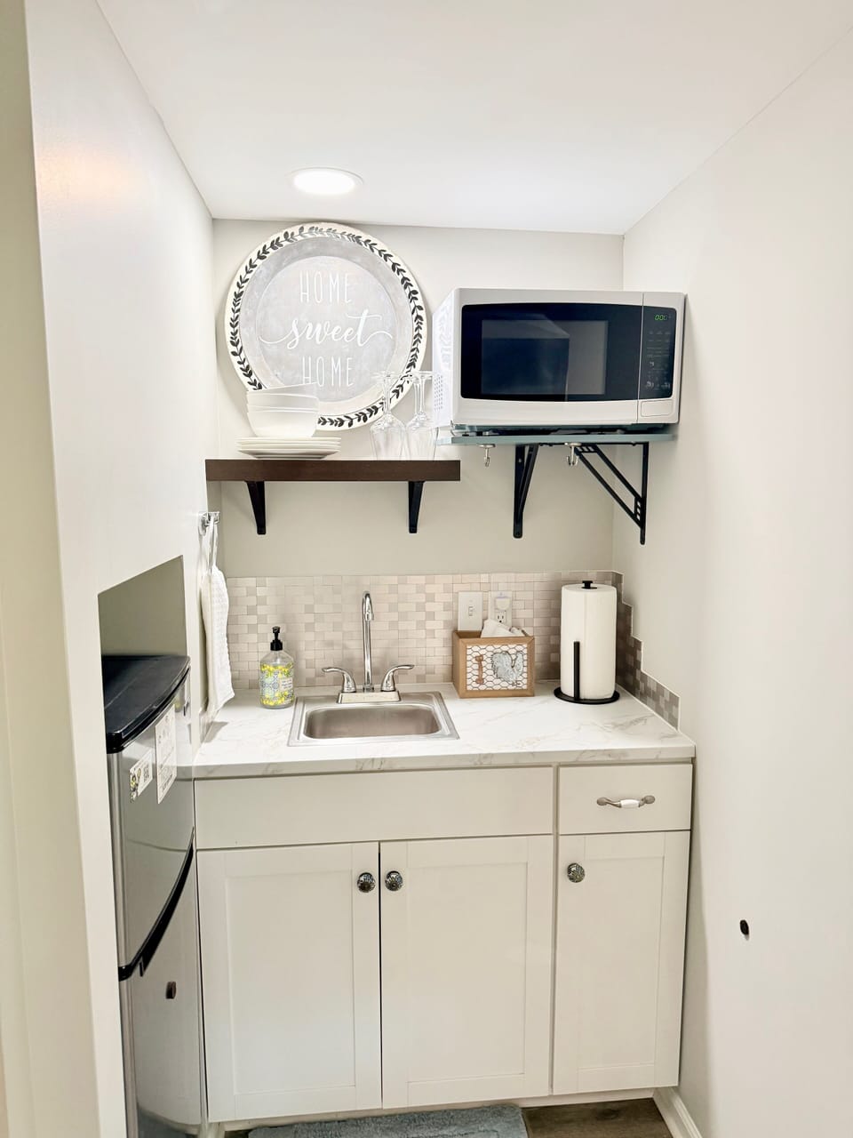 Kitchenette with microwave, mini fridge, plates, bowls, wine glasses & utensils.