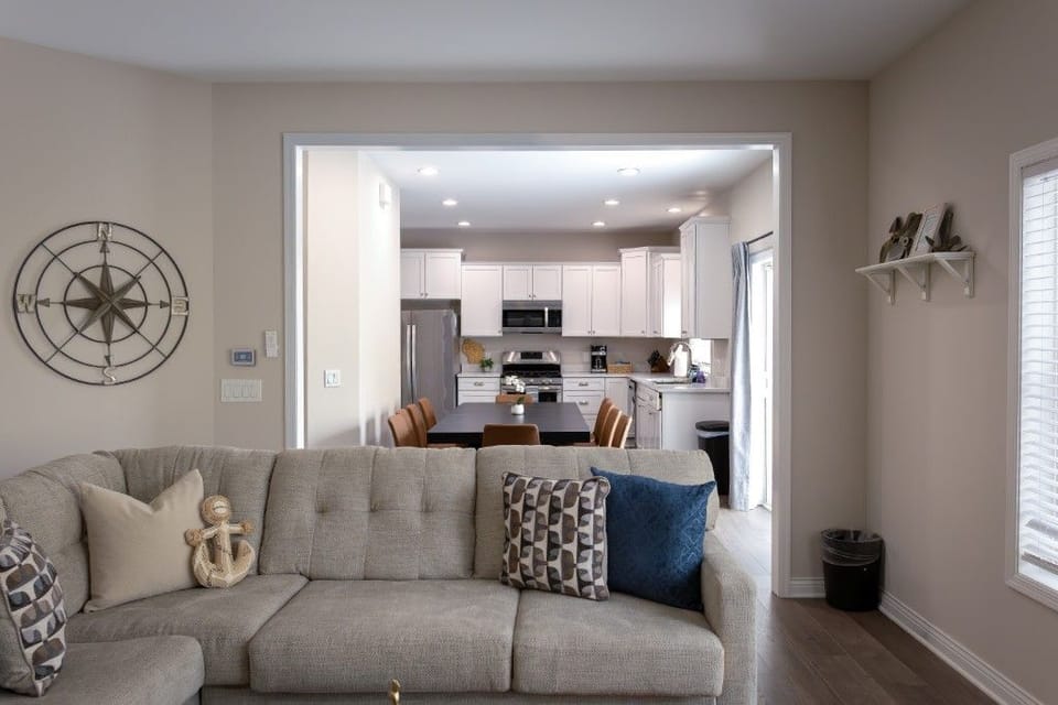 The open-layout living room, complete with a plush sofa and a glimpse of the dining area, conveys a seamless blend of comfort and elegance, making it ideal for family gatherings and cherished moments.