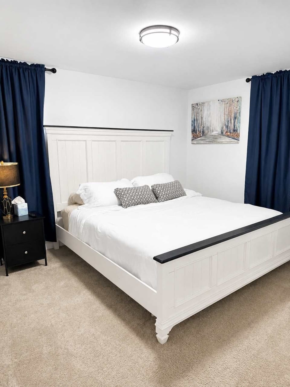 Bright and cozy bedroom featuring a plush white bed, crisp linens, navy curtains, warm bedside lighting, and calming wall art—perfect for relaxing after a day of exploring.