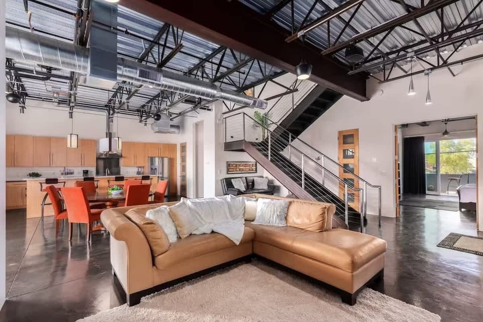 Welcoming living area with a bright, open-concept layout, a beige leather sectional, a smart TV in the entertainment center, and an industrial-style exposed ceiling.
