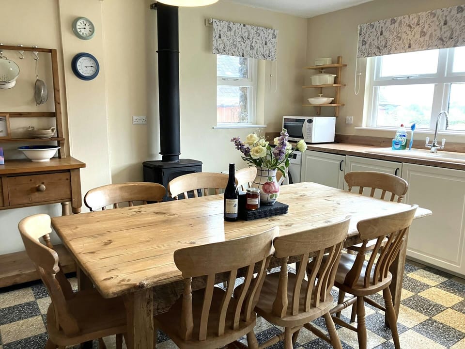 Dining table with eight chairs, stove pipe and two windows