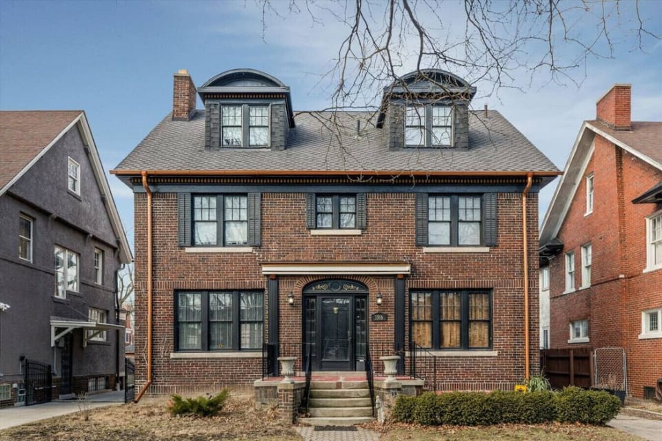 A grand historic home spread across three levels, surrounded by lush greenery and rich in old-world charm.