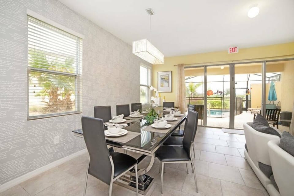 Welcome to our welcoming dining area featuring a sleek glass table, ideal for unforgettable meals. The warm yellow walls and modern lighting create a cheerful ambiance, enhanced by large sliding doors that invite in natural light.