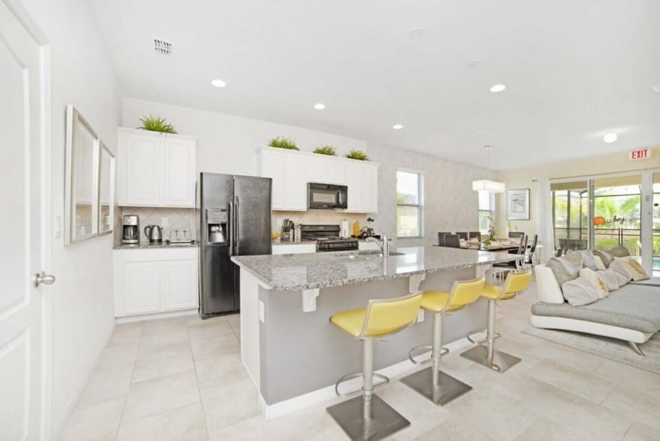 This bright and airy kitchen boasts sleek granite countertops and modern cabinetry, enhanced by cheerful yellow bar stools. The open layout connects effortlessly to the living area, ideal for both entertaining and relaxing.