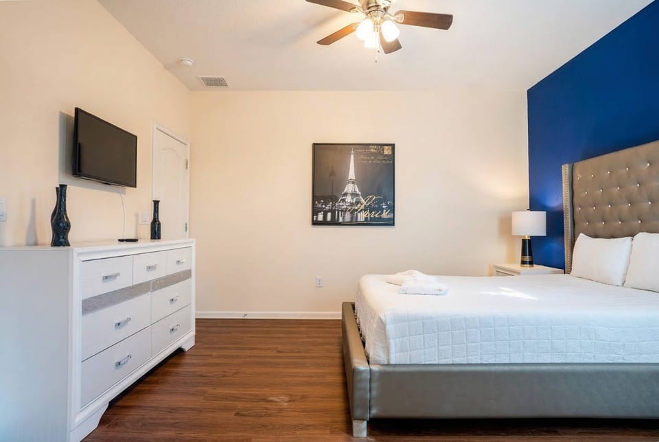 This stylish bedroom boasts a sleek gray bed with crisp white linens, a chic deep blue accent wall, and warm wood flooring, all bathed in natural light, creating a sophisticated and inviting atmosphere for your stay.