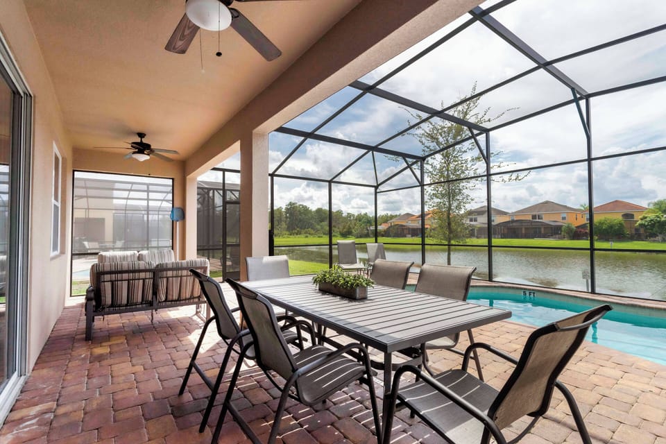 Enjoy the charming covered patio with a spacious dining table and cozy seating, ideal for outdoor meals. Relax with serene water views through the screen enclosure, complemented by inviting rustic brick flooring.
