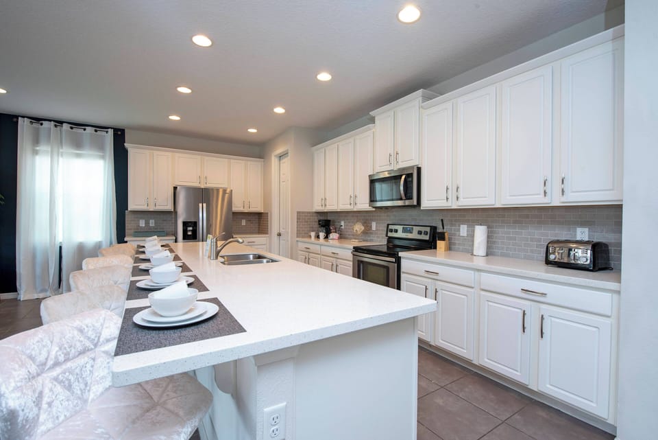 Welcome to this bright kitchen with sleek white cabinetry and a spacious island ideal for meal prep or casual dining. The stainless steel appliances shine under soft lighting, inviting you to explore your culinary creativity.