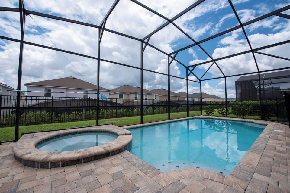 Experience your private oasis with a sparkling pool and soothing hot tub, all set on spacious paver decking. The screened enclosure provides stunning views of lush greenery, inviting you to relax and unwind under the open sky.