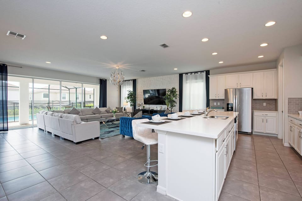 Enjoy a relaxing stay in this bright, open-plan living area with a spacious kitchen featuring sleek white cabinetry and a modern island. Large windows flood the space with natural light, creating a warm and inviting atmosphere.
