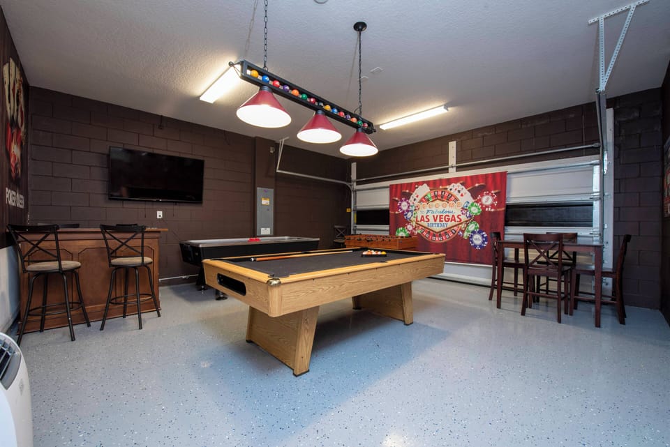 Welcome to our lively game room, where stylish brown walls and a sleek pool table set the stage for friendly competition. Gather in the cozy bar area, lit by colorful pendants, for a fun and relaxed atmosphere.