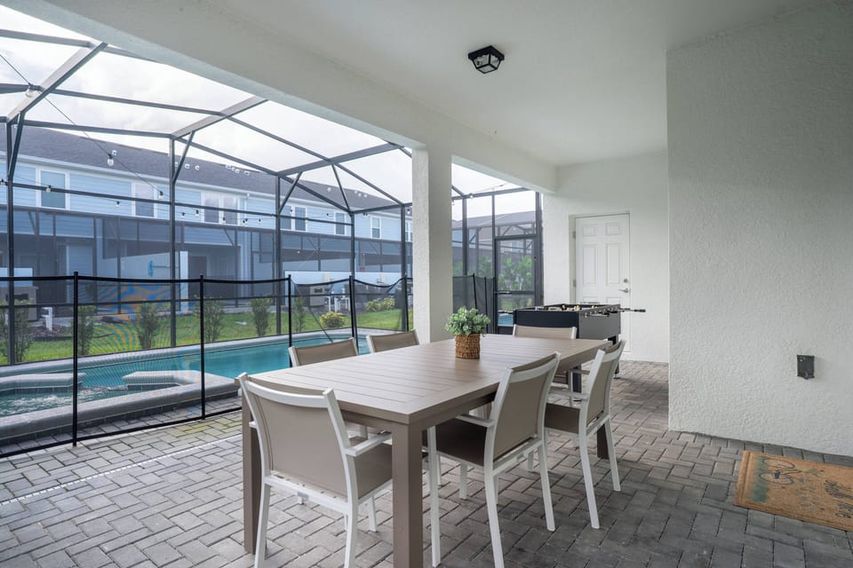 Step onto the screened patio featuring a stylish wooden dining table and modern chairs, where you can enjoy tranquil views of the private pool surrounded by lush greenery, ideal for relaxation and outdoor dining.
