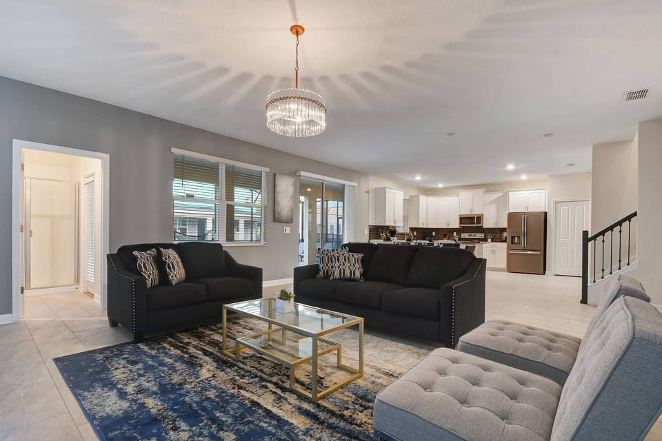 Experience a stylish living area with plush dark sofas perfect for relaxation, a chic glass coffee table, and a vibrant rug. Large windows fill the space with natural light, creating a warm and inviting atmosphere for your stay.