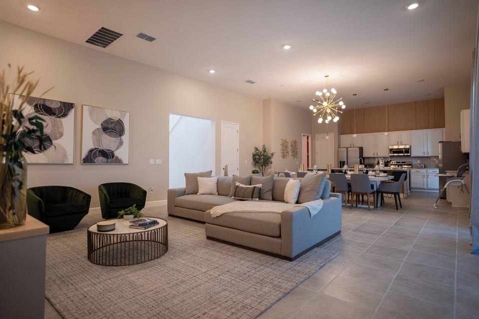 Experience a spacious living area that blends contemporary design with comfort, featuring a cozy beige sectional and stylish green armchairs, all illuminated by warm lighting for a welcoming atmosphere ideal for relaxed evenings.