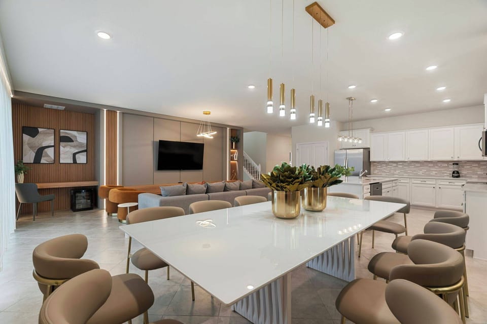Experience our inviting dining area with a sleek white table and cozy rounded chairs perfect for gatherings. Elegant pendant lights add warmth to the modern decor, seamlessly connecting to the kitchen for a delightful atmosphere.