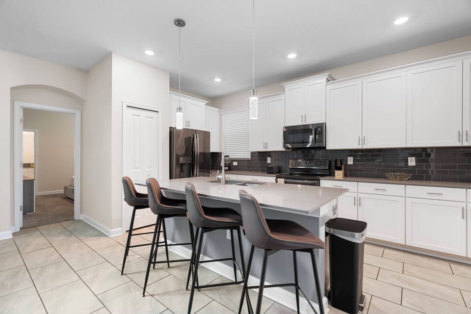 Discover culinary bliss in this spacious kitchen with sleek white cabinetry and a striking dark backsplash. The inviting island with modern bar stools is perfect for casual meals or enjoying your morning coffee.