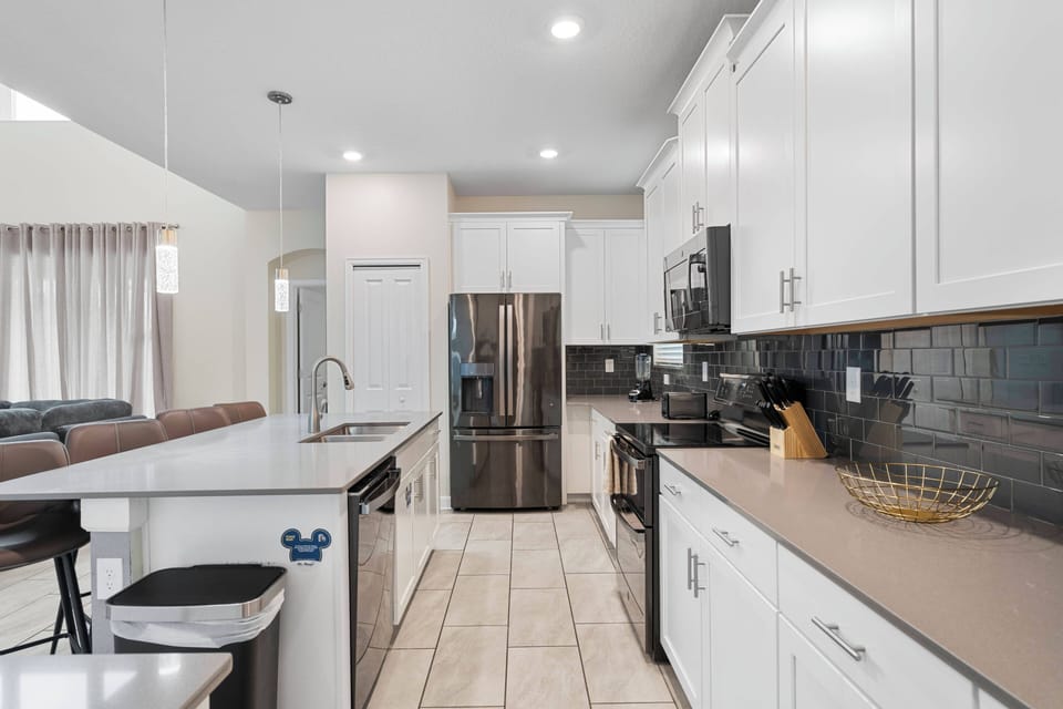 This bright kitchen features sleek white cabinetry paired with a striking dark backsplash, creating a stylish contrast. Enjoy the spacious layout that seamlessly connects to the living area, perfect for socializing while cooking.