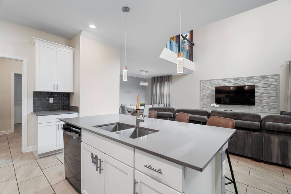 Enjoy a stylish kitchen featuring sleek white cabinetry and a spacious island, ideal for meal prep or casual dining. Modern appliances and warm lighting create a welcoming atmosphere for your stay.