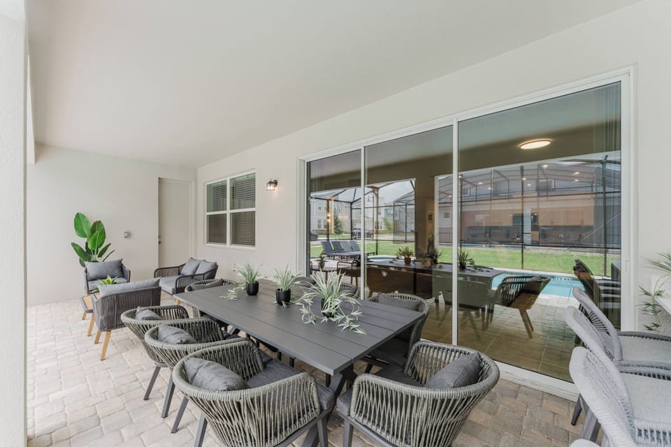 Step outside to a charming covered patio, where a sleek dining table surrounded by stylish wicker chairs invites alfresco meals. Sunlight filters through expansive glass doors, offering a seamless view of the lush outdoor space.