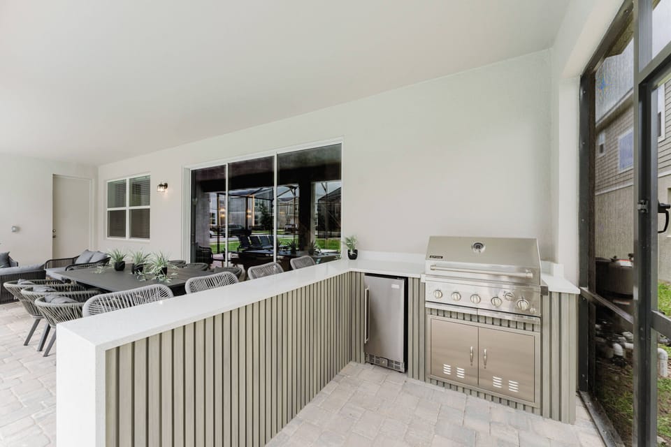 Step outside to a chic al fresco dining area with stylish rattan seating and a built-in grill, ideal for evening barbecues. Large windows flood the space with natural light, seamlessly connecting you to the lush greenery outside.