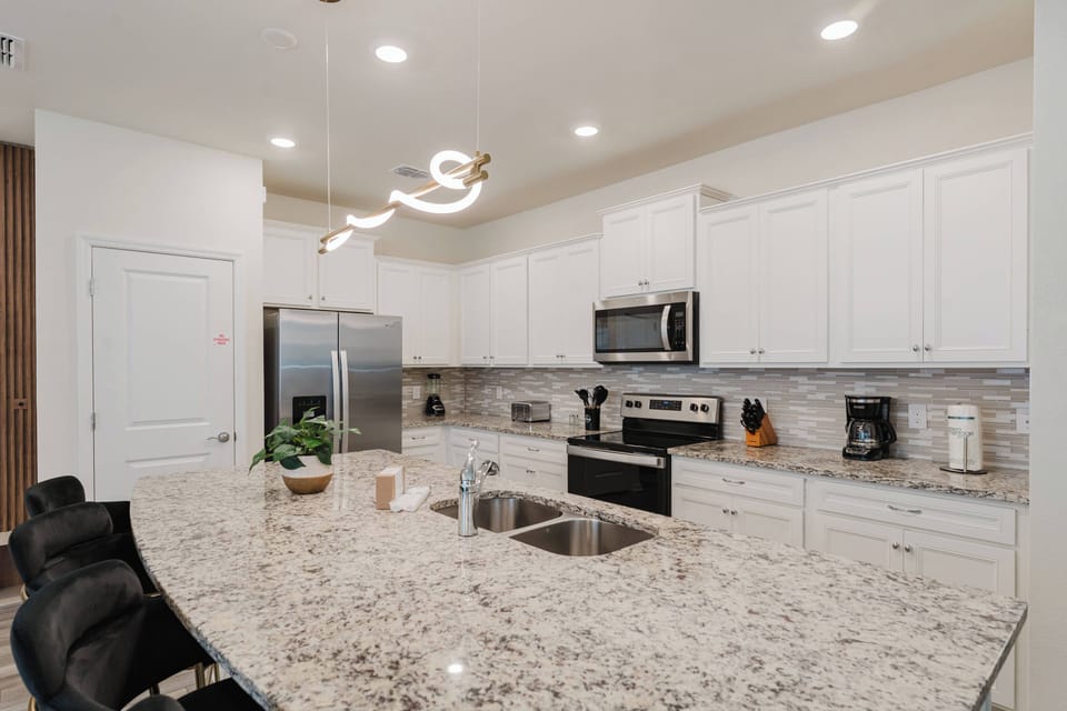 Step into a beautifully designed kitchen featuring sleek white cabinetry and a spacious granite island, perfect for meal prep or casual dining. The modern lighting adds a warm glow, making this space ideal for culinary creativity.