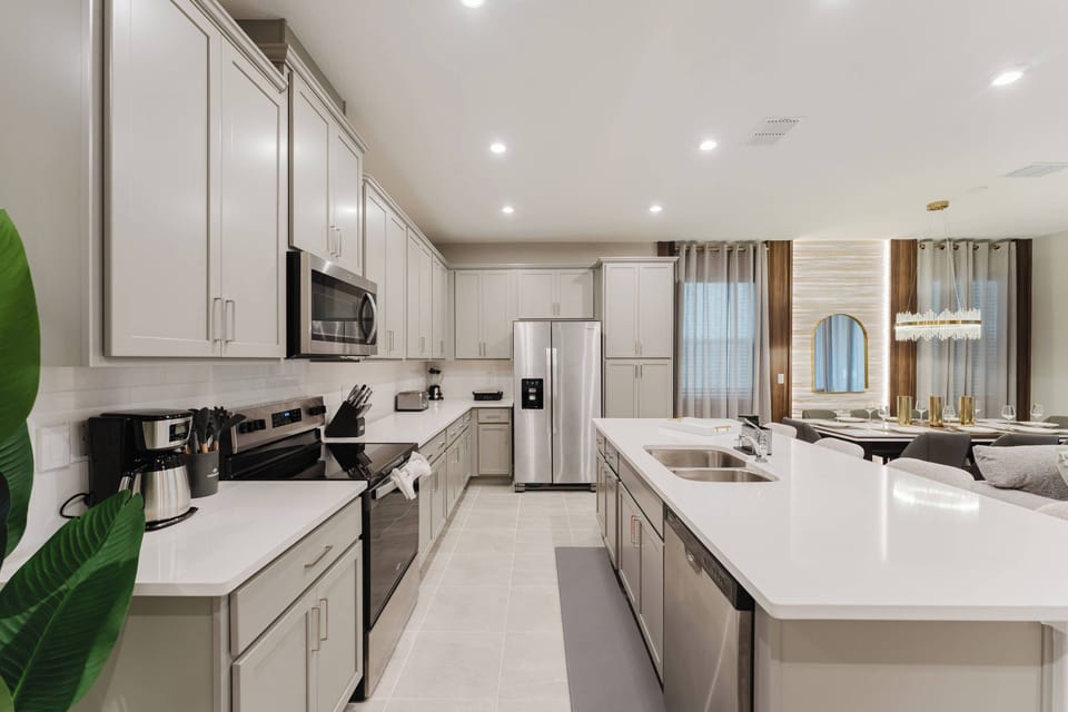 This stylish kitchen features sleek white cabinetry and a spacious island perfect for meal prep or casual dining. Modern stainless steel appliances add sophistication, and large windows fill the space with inviting natural light.