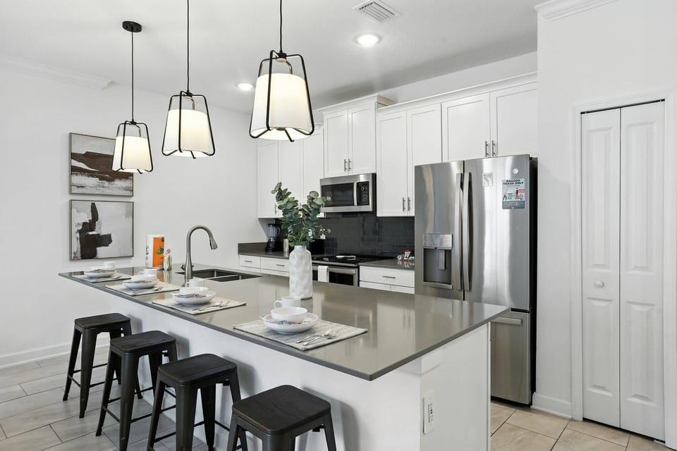 This chic kitchen features sleek gray countertops and modern black bar stools, ideal for casual dining. The stylish pendant lighting adds to the bright, open atmosphere, creating a perfect setting for your culinary creativity.