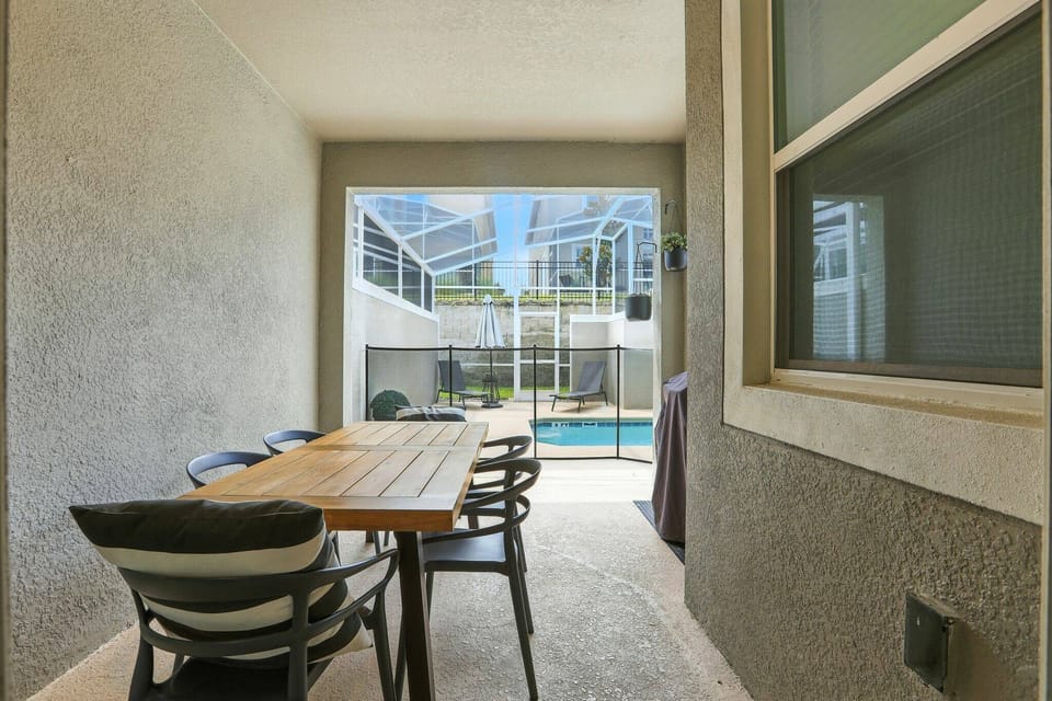 Step outside to your private outdoor dining area, where a sleek wooden table invites you to enjoy meals al fresco. Surrounded by a screen enclosure, this space offers a seamless view of the sparkling pool, perfect for relaxation.