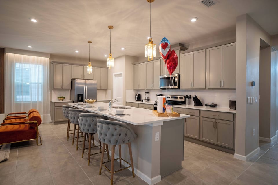 Step into this stylish kitchen, where sleek gray cabinetry meets chic pendant lighting. The spacious island, adorned with plush stools, invites casual dining, while the warm glow from the windows enhances the inviting atmosphere.