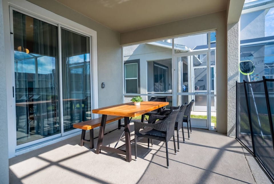 Enjoy outdoor dining in a covered screened patio with a wooden table, black wicker chairs, sliding glass doors, and natural light, creating a comfortable space for family meals during vacation.