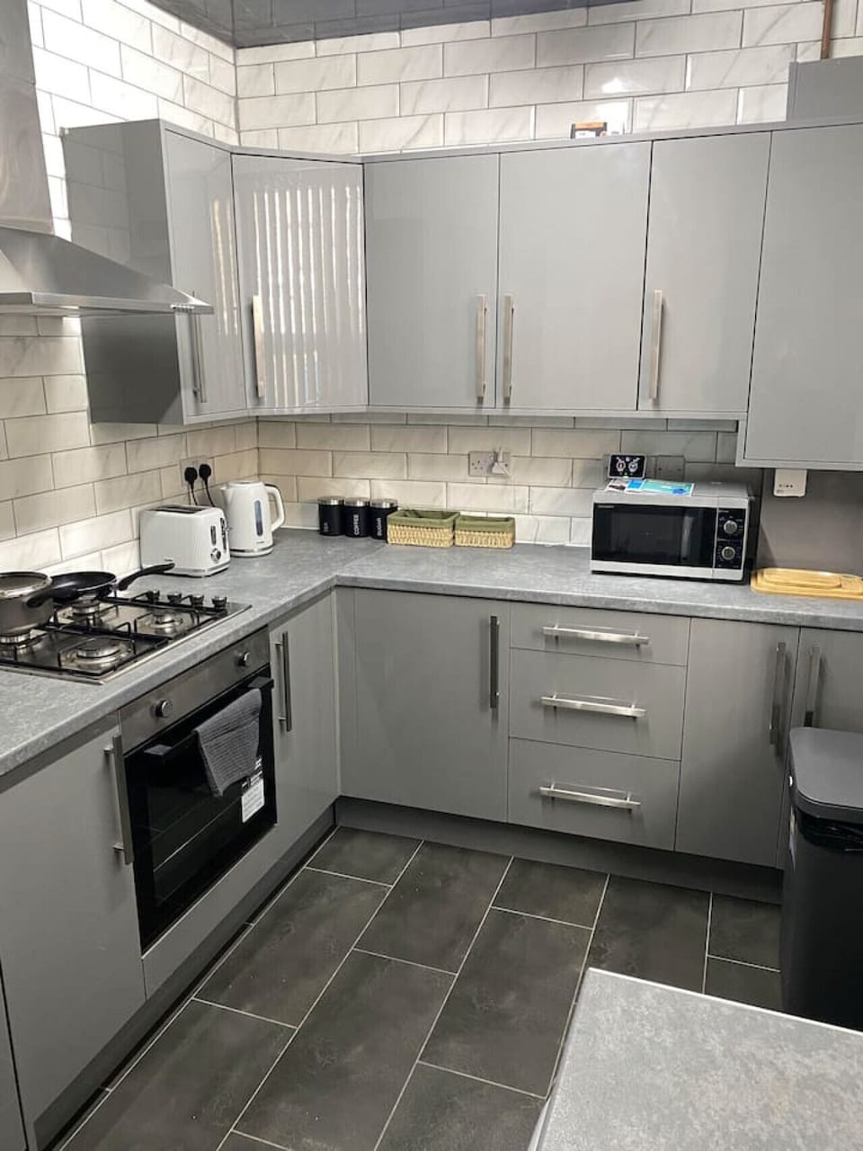Full kitchen view with L-shaped counters, hob, oven, and microwave.