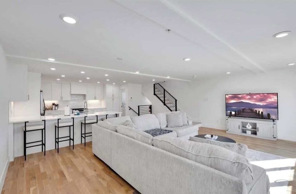Spacious open living area with a large sectional sofa, big TV, hardwood floors, and direct access to the kitchen—perfect for relaxing and gathering.