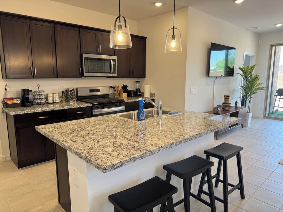 Kitchen island with stools, dark cabinets, pendant lights, and TV