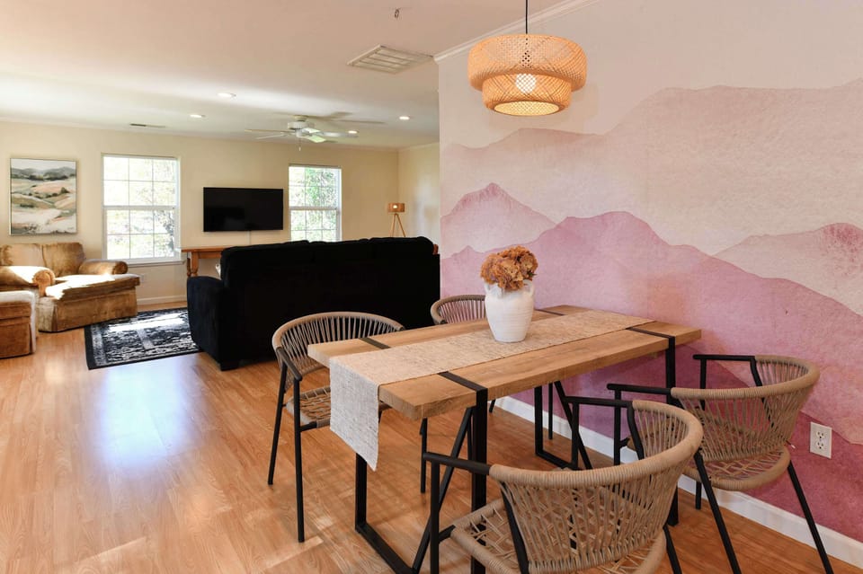 Stylish dining space with natural wood table, woven chairs, and a charming mural that adds character and warmth.