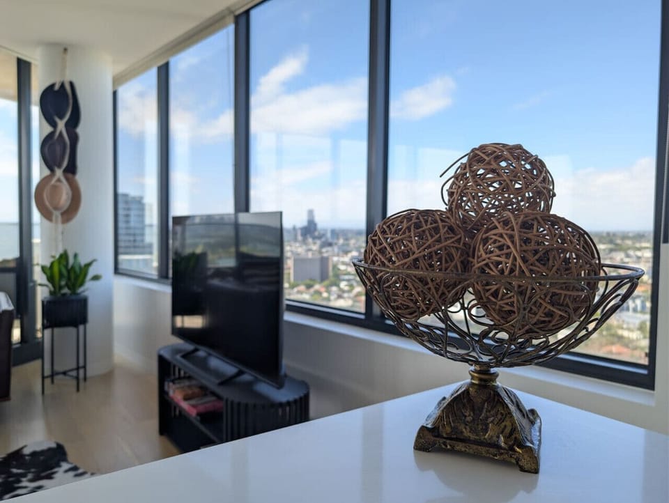 A decorative rattan centrepiece on the kitchen counter, with the living room and sweeping city views stretching out behind it. A glimpse of how the apartment balances personality with an ever-present connection to the skyline.