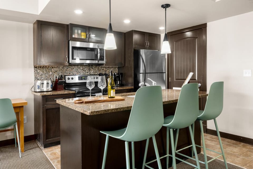 This fully equipped kitchen shines with sleek appliances, ample countertop space, and a breakfast bar with comfortable seating for three, perfect for casual meals and morning gatherings.  *Pastries added for photoshoot purposes.*