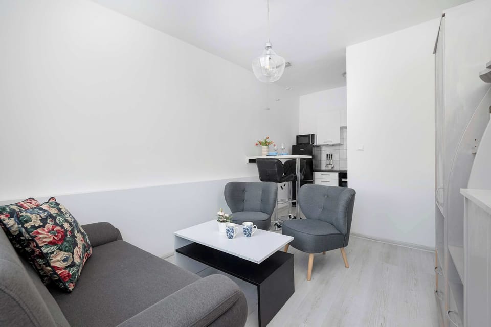 A living room corner with a gray sofa and a small coffee table. Minimal decor keeps the space uncluttered. Light flooring enhances the brightness.