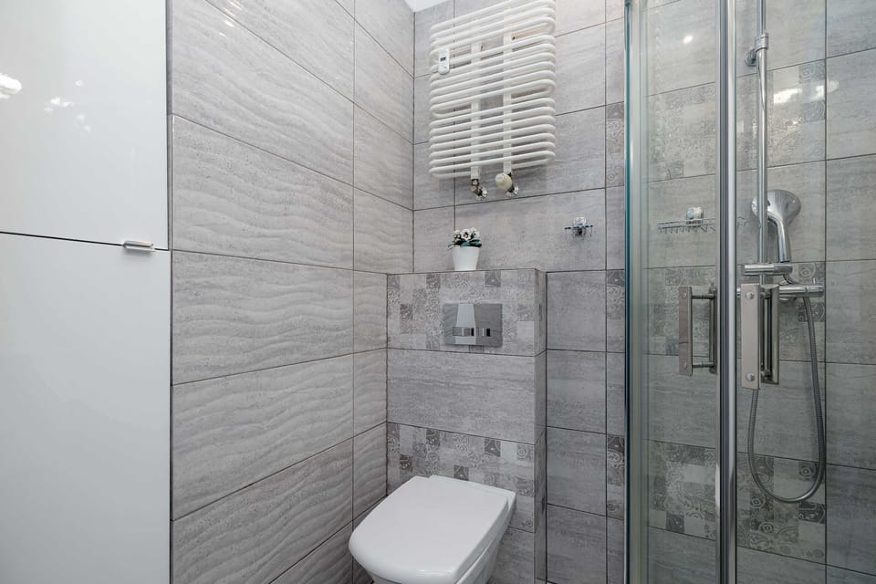 A bathroom view with a toilet and shower cabin. Gray tiles create a cohesive look. The space feels functional and well maintained.