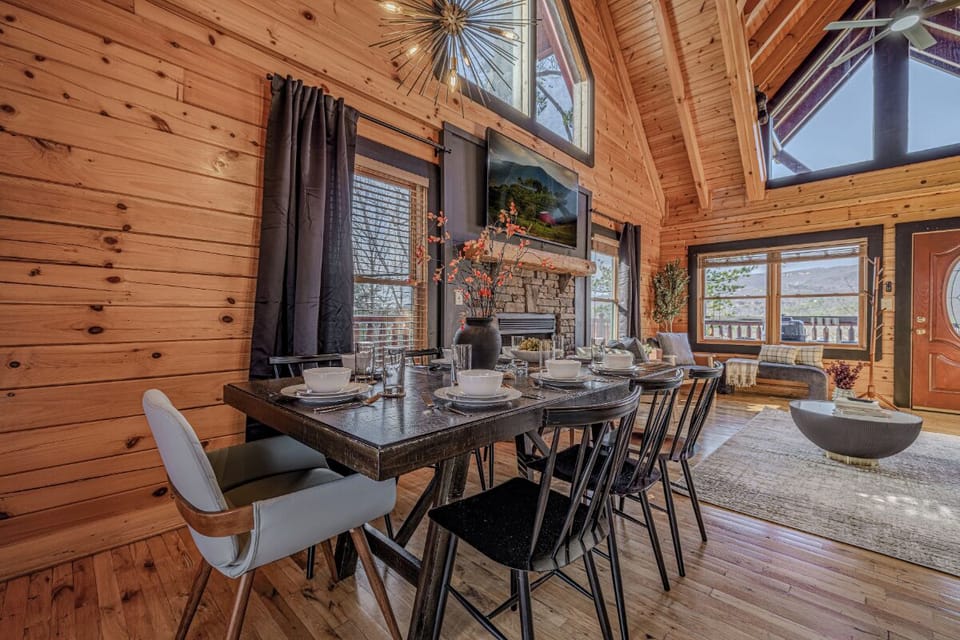 Gather around your rustic dining table beneath soaring cathedral ceilings, where warm wood walls and cozy fireplace create perfect moments for sharing meals together.