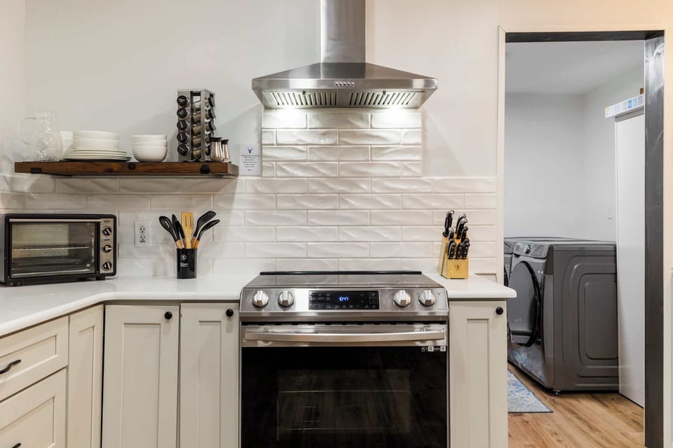 A fully outfitted farmhouse kitchen with a stainless range, professional hood vent, spice rack, and direct laundry room access — everything a group of 10 needs for a comfortable Pocono stay.